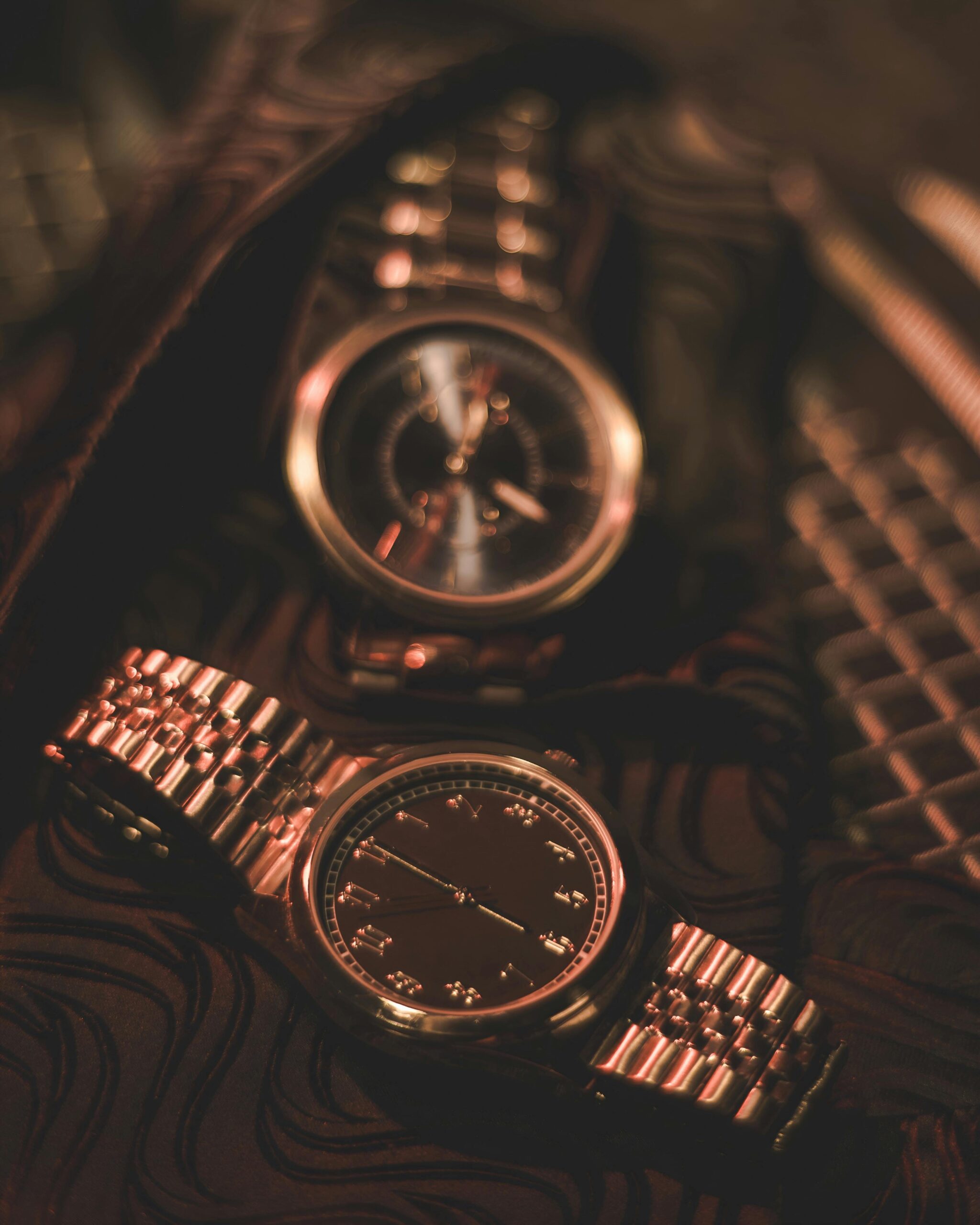 Close-up of two stylish wristwatches with metal bands under warm lighting, showcasing detailed watch faces
